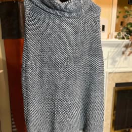 Gray knit turtleneck sweater hanging against a background.